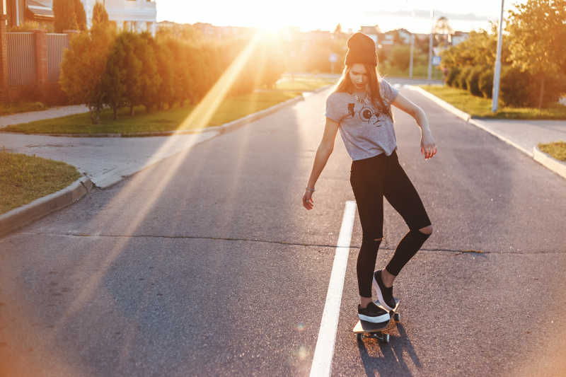 夕阳下在马路上踩着滑板的年轻女孩