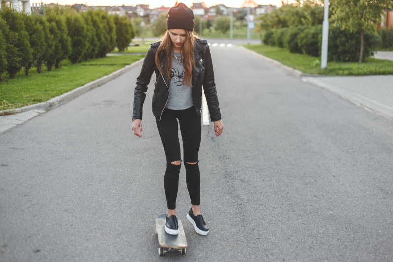 在马路上踩着滑板的年轻女孩