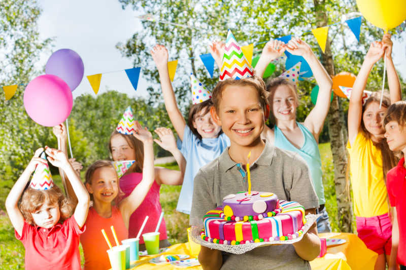 快乐的小男孩在生日聚会上站在朋友中间捧着生日蛋糕