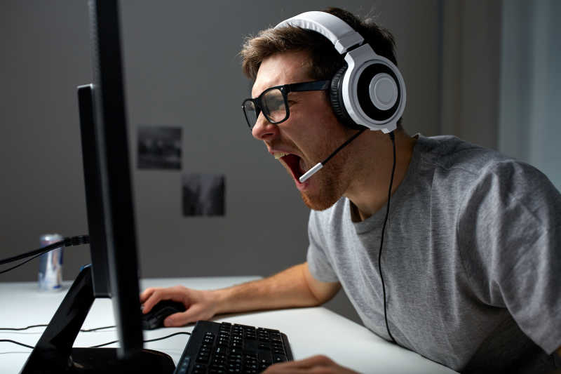 戴着耳机愤怒玩电脑的年轻男人