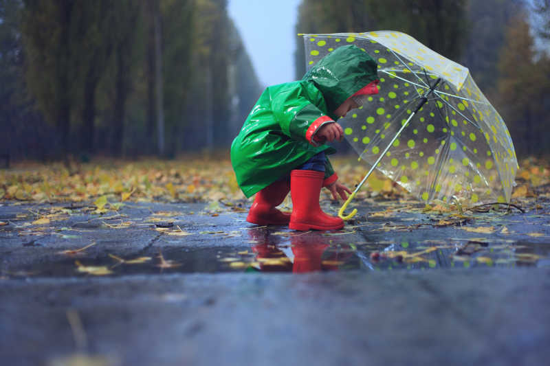 雨后的公园有个小孩撑着伞在玩耍
