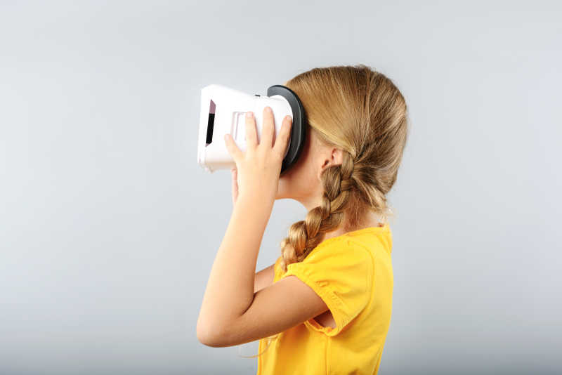 灰白色背景下戴着虚拟现实耳机的黄衣小女孩