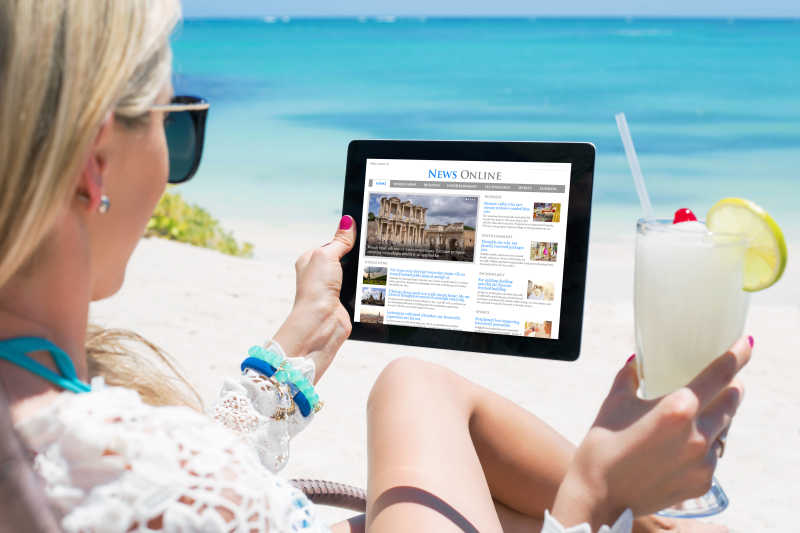 在海滩上放松的女子使用平板电脑看新闻