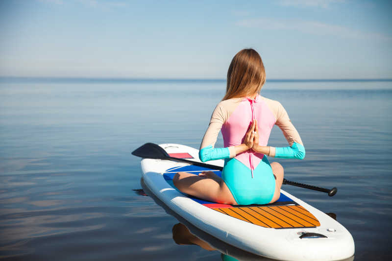 女子在水面瑜伽板上用船桨做瑜伽