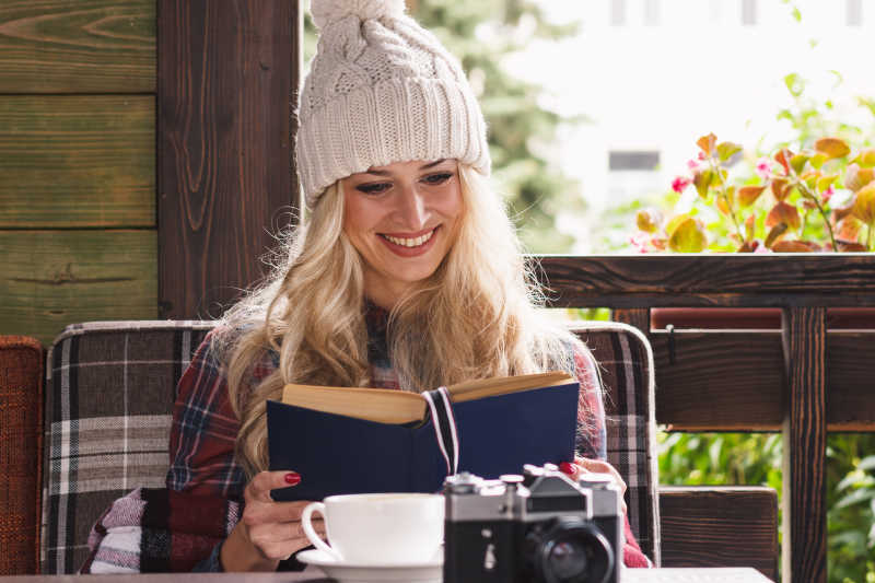 戴着帽子的年轻金发女郎坐在咖啡馆里看书