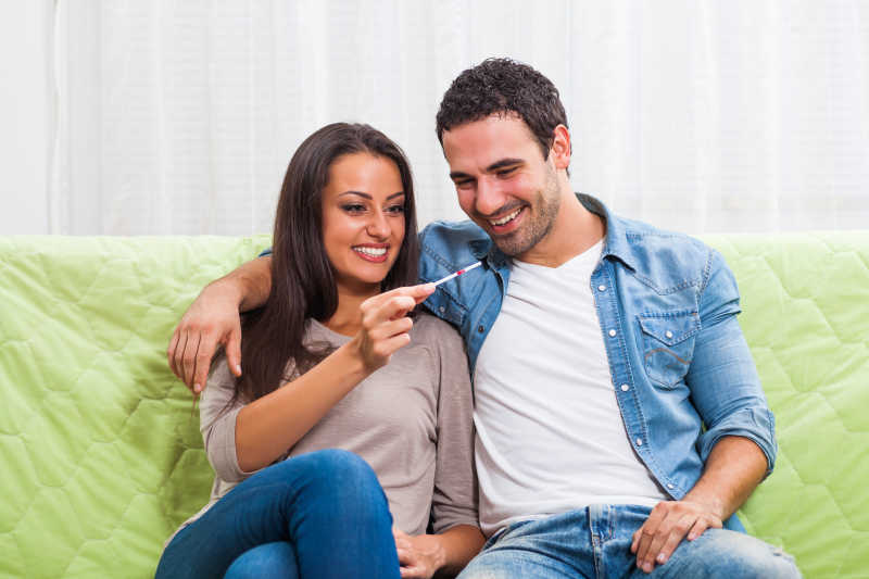 沙发上年轻夫妇微笑的看着阳性妊娠试验结果