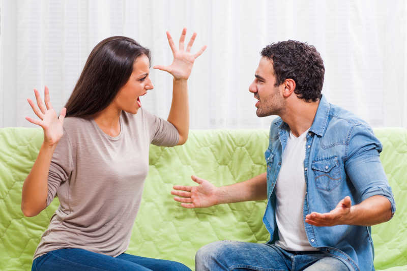绿色沙发上面对面争吵的年轻夫妇