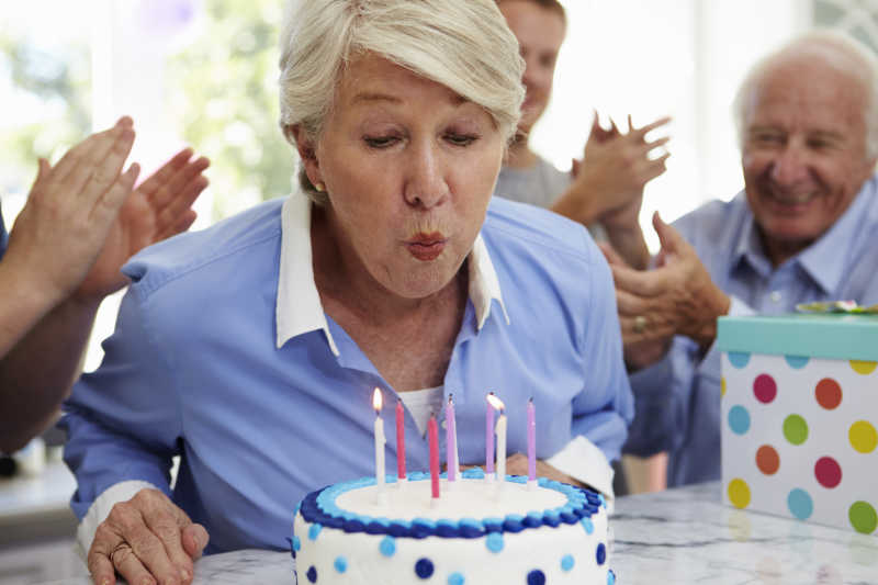 吹灭生日蛋糕蜡烛的高龄妇女