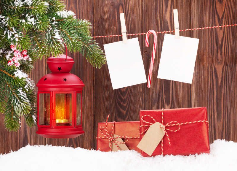 木板背景下雪地上的圣诞蜡烛灯笼礼品盒及空白照片