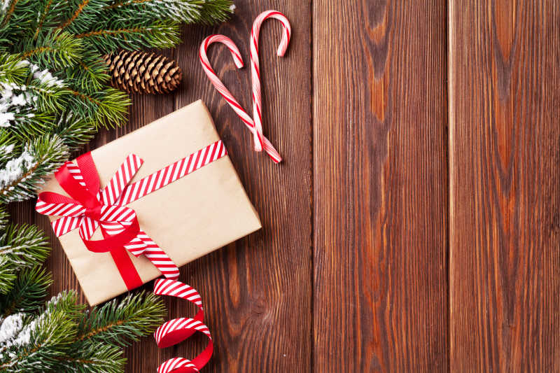 木纹理桌上的拐杖糖红色丝带礼品盒和圣诞树枝