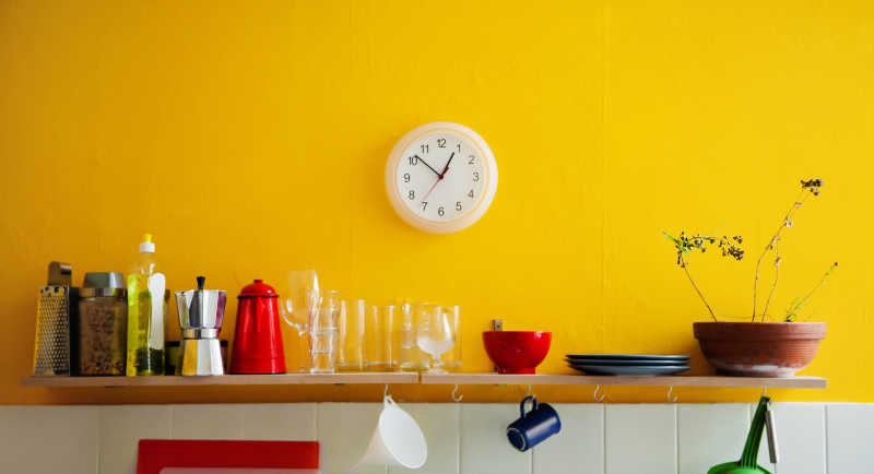 黄色墙壁架子上的炊具和墙上的钟表