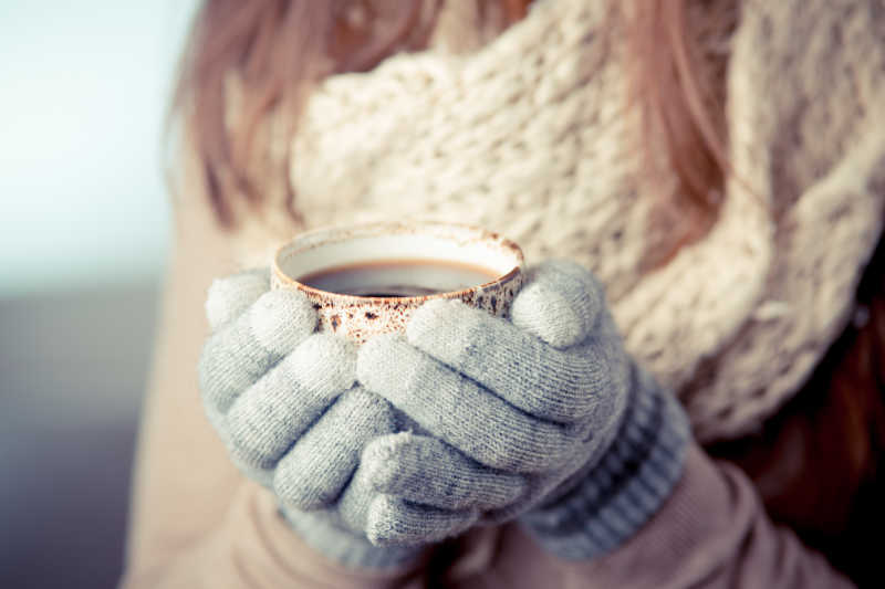 戴手套的年轻女子拿着咖啡杯