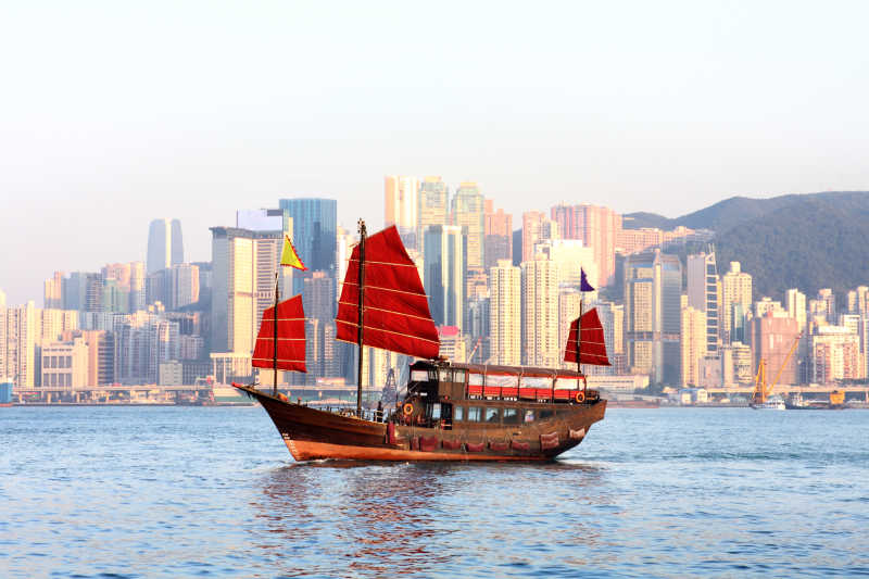 香港大楼背景下水上的红色拉货帆船