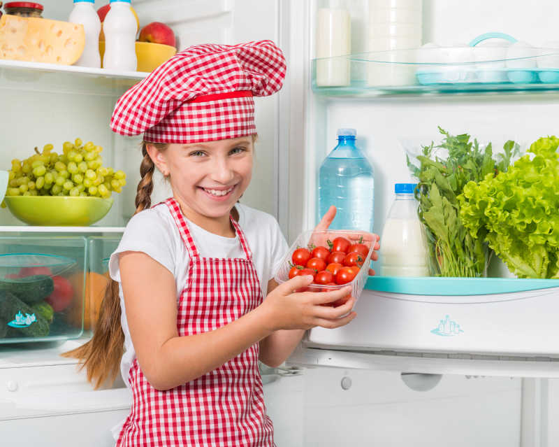 冰箱旁边的小厨师拿着西红柿
