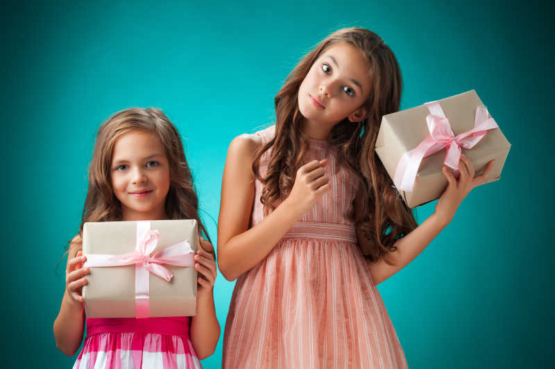 蓝绿色背景下包着礼品盒的两个小女孩