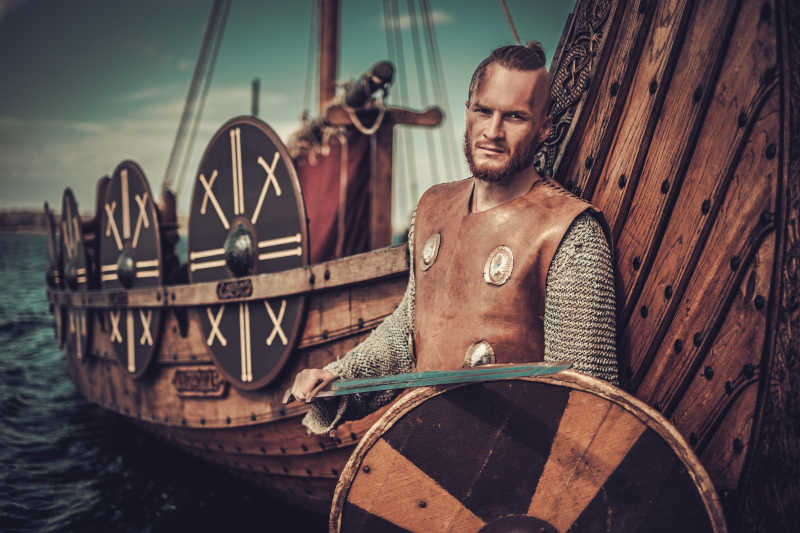 手持剑和盾牌靠在海边船头的维京勇士
