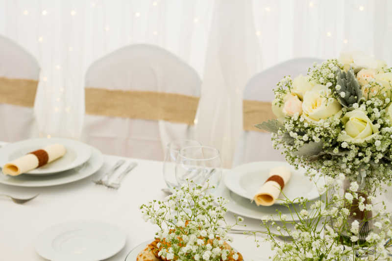 白色背景下结婚餐桌上的餐具和满天星花朵装饰