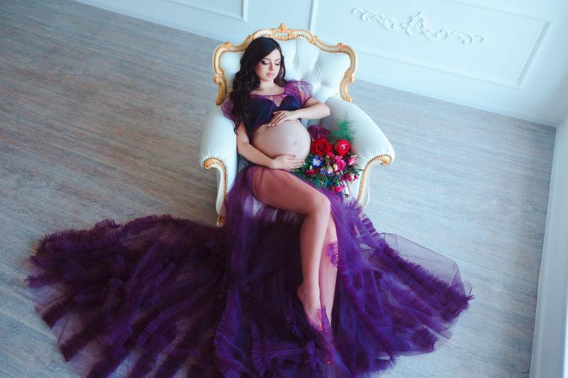 白色椅子上的穿紫色服装的时尚孕妇