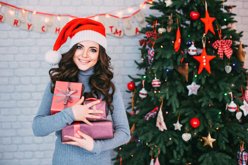 抱着礼盒站在圣诞树旁的年轻美女