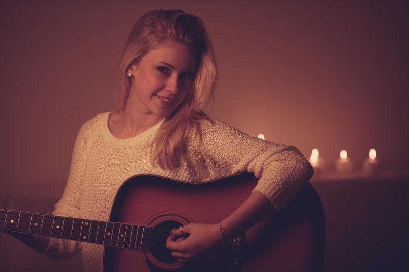 美丽的金发女人在烛光下弹吉他