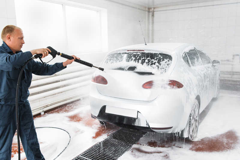 白色室内男人使用高压水枪冲洗车上的泡沫