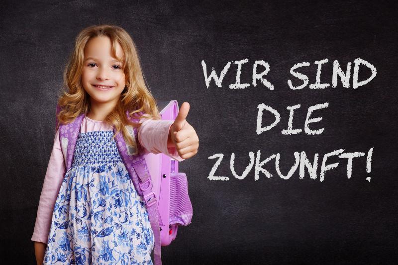 写着字的黑板前伸出大拇指的背着书包的小女孩