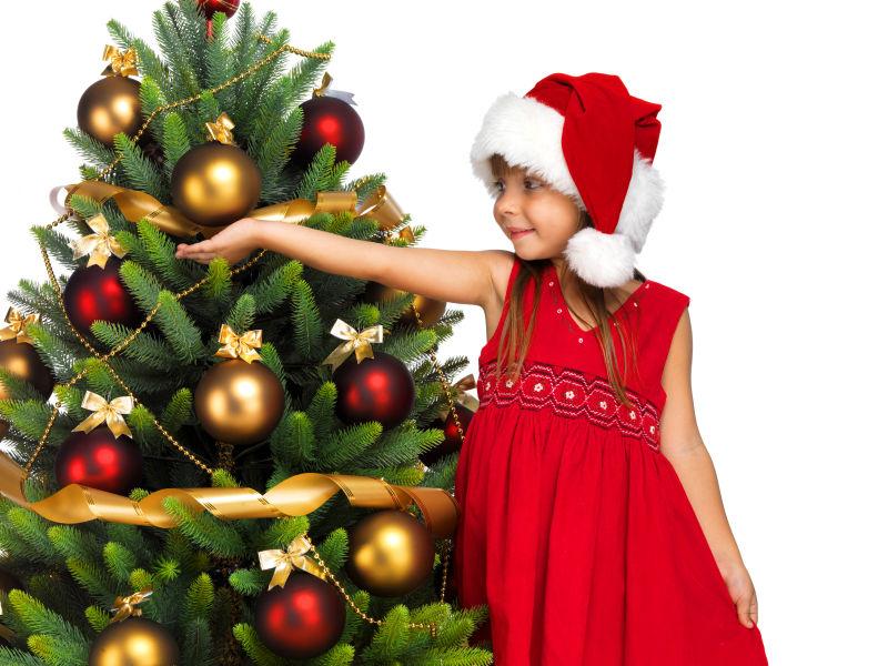 戴着圣诞帽的小女孩站在圣诞树旁边