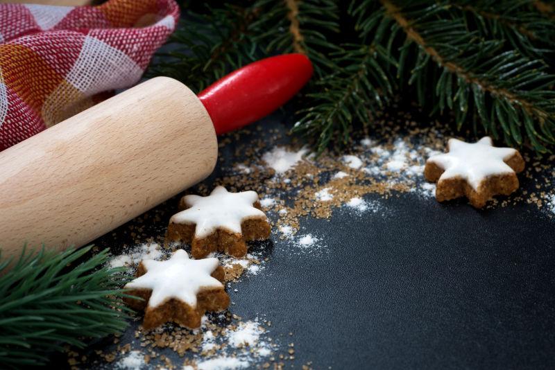 圣诞树枝背景下的黑色桌上的擀面杖和姜饼