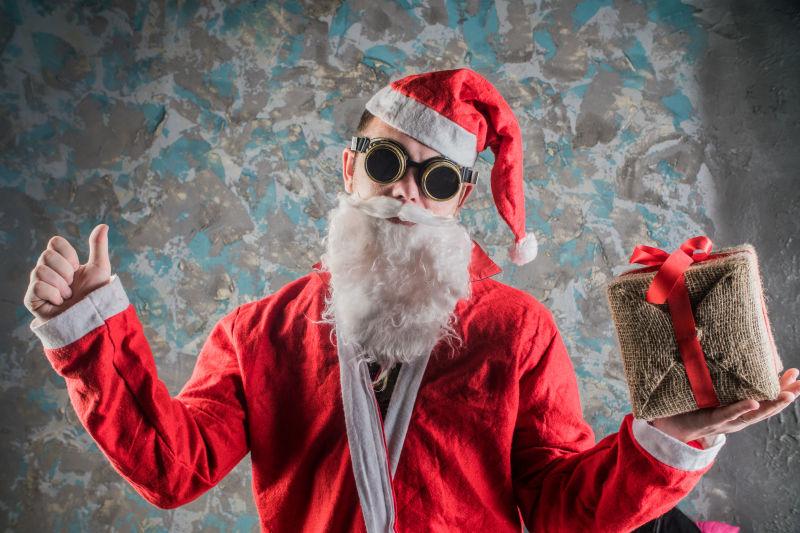 蓝色花纹的水泥墙背景下戴着搞笑眼镜拿着礼物的圣诞老人
