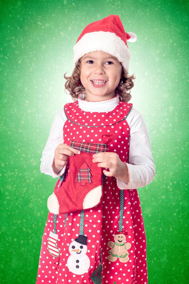 绿色背景下戴着圣诞帽子拿着袜子的小女孩