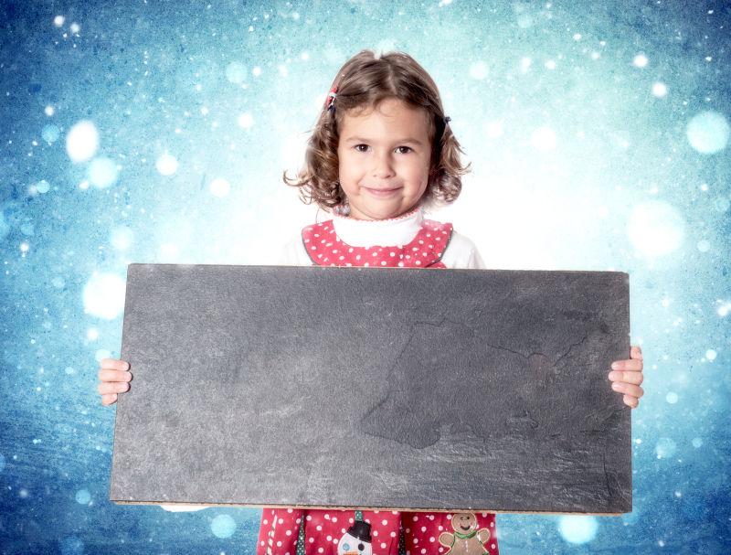 浅蓝色星空背景下穿着圣诞礼服抱着小黑板的小女孩