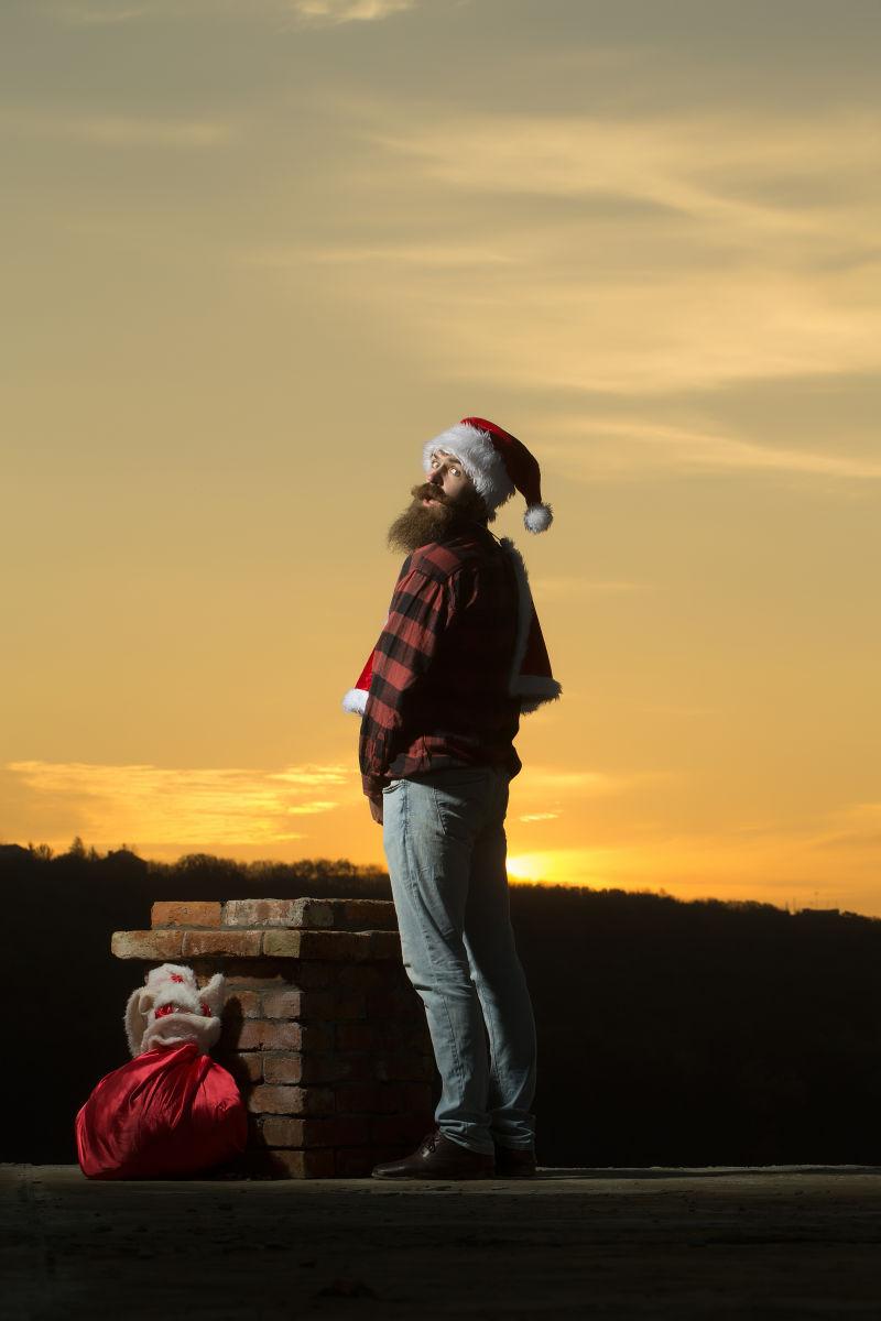 圣诞老人装扮的年轻长胡子男子在砖烟囱旁小便