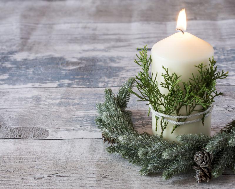 木地板上挂着绿色植物和假枞树枝的美丽的白色蜡烛