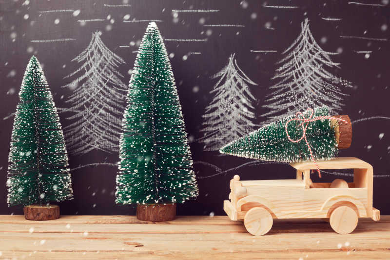黑色背景下木桌上的小木玩具车上的圣诞树