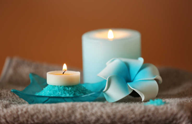 褐色背景下亚麻布上的白色蜡烛和浅蓝色花朵