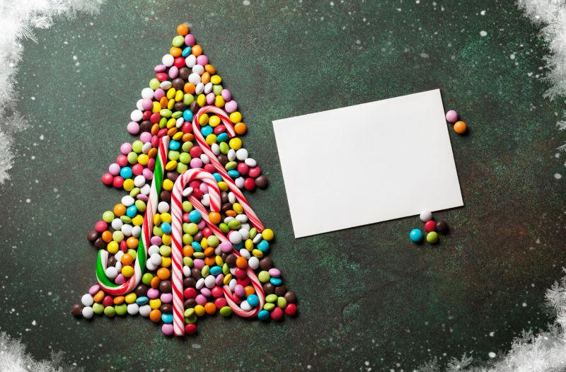 浅绿色桌上摆成圣诞树形状的彩虹糖和拐杖糖
