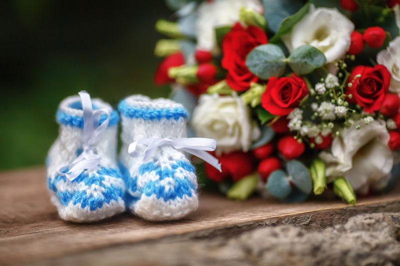 木制背景下的婚纱的红玫瑰和蓝色婴儿靴