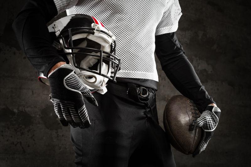 黑色背景上拿着橄榄球和头盔的运动员