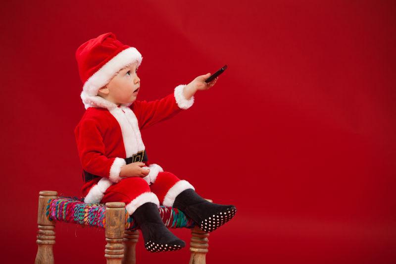 可爱的孩子穿着圣诞老人克劳斯的衣服坐在椅子上