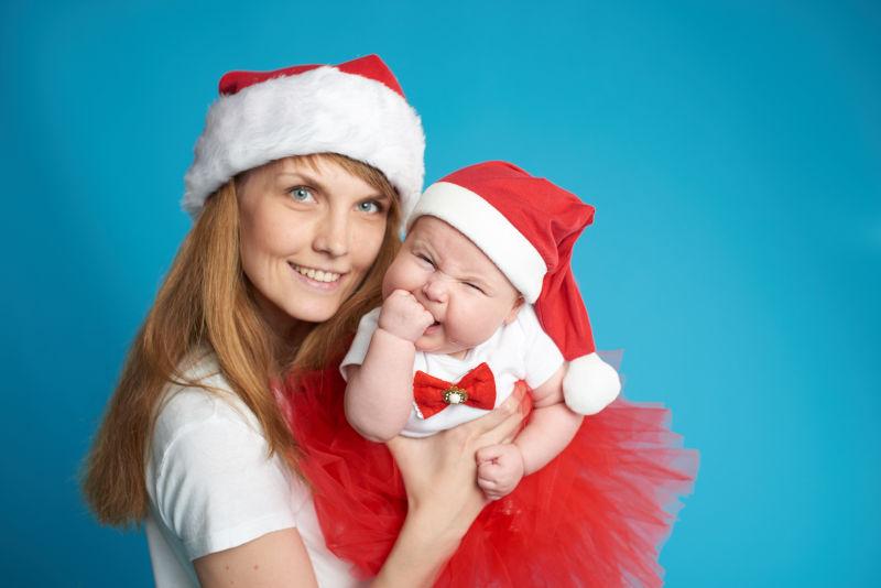 快乐的年轻母亲带着甜蜜的婴儿戴着圣诞帽