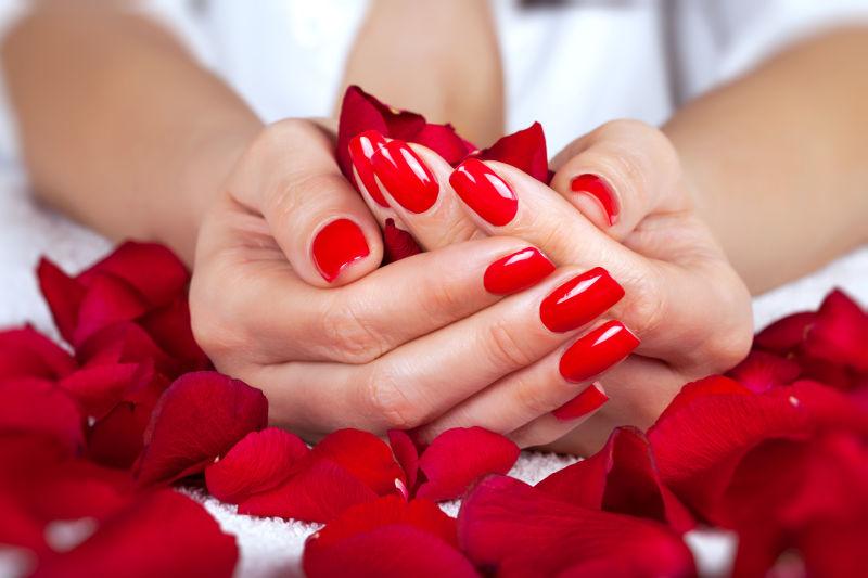 染着红色指甲的女性捧着玫瑰花瓣