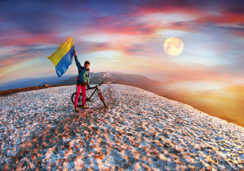 极限自行车运动员在山顶挥舞旗帜