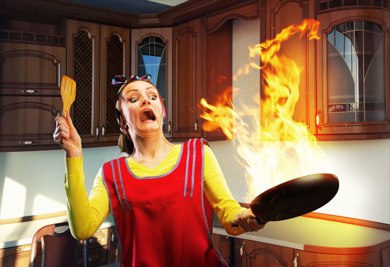 厨房里家庭妇女拿着起火的平底锅面露惊慌表情