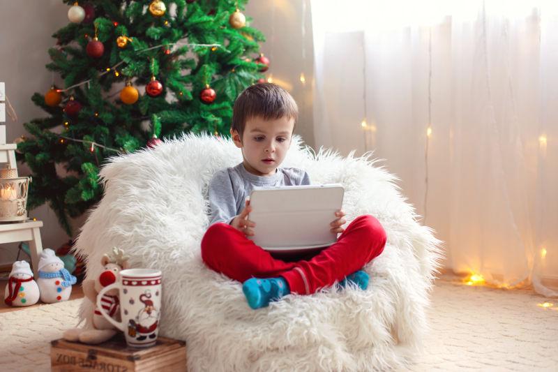 在圣诞节树下坐在豆袋上的小男孩看平板电脑