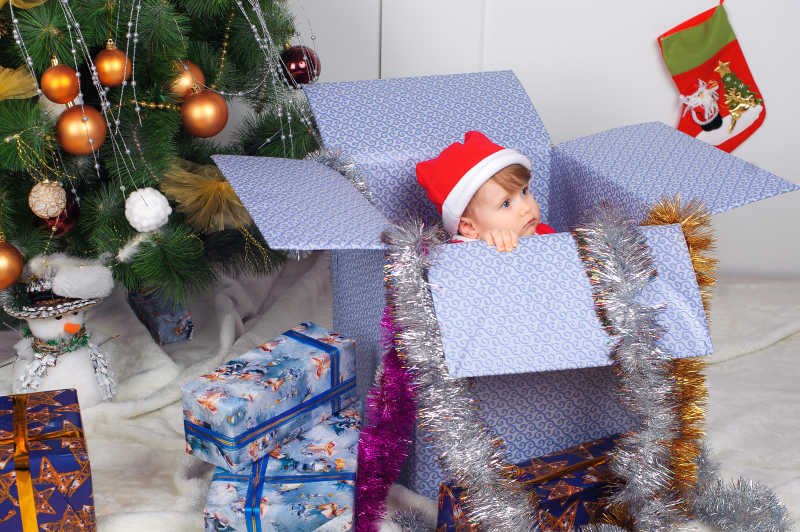 圣诞树下礼物盒子里有个可爱的小孩子