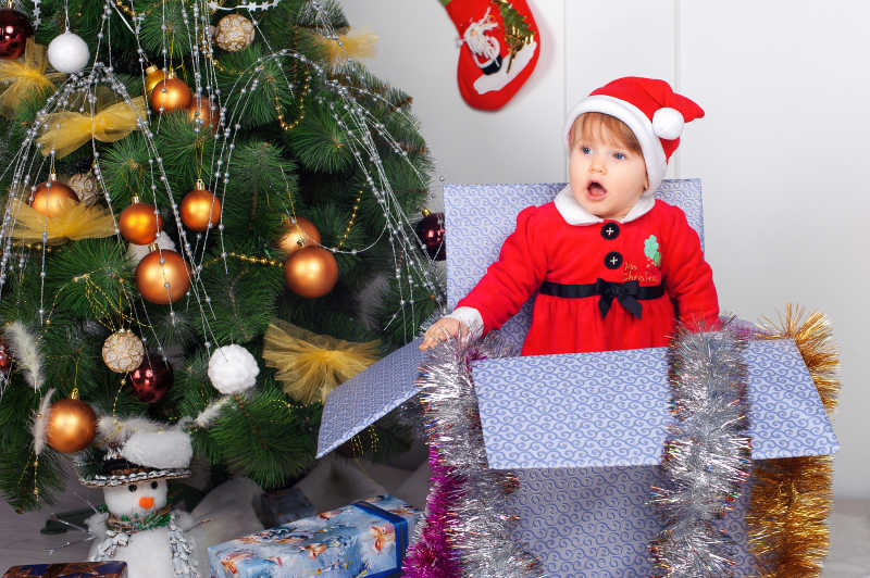 圣诞树边的礼物盒里的可爱小女孩