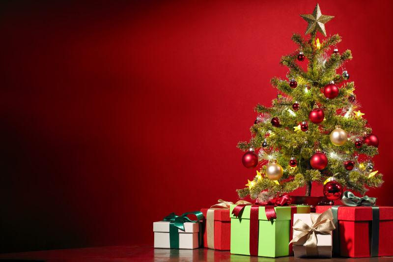 红色背景下挂满小球的圣诞树和多样礼物